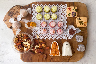 「おばけギフト(L)」のハロウィン限定スイーツが木製ボードに美しく並べられた写真。 緑茶や紫芋味のサブレの周りには、ナッツやゴースト型のフロランタン、エディブルフラワーとハーブがトッピングされた米粉サブレ、 キャラメル包みのアマレッティ、アルミで包まれたラム酒のベイクドショコラを配置しています。