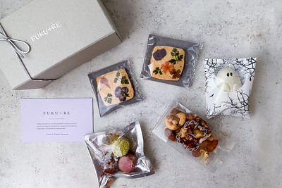 FUKU+REブランドのギフトボックスと、花の押し花クッキー、ナッツ、カラフルな焼き菓子、ゴースト型の和菓子を黒白模様の皿に盛り付けた上品なハロウィン限定お菓子詰め合わせギフトの写真