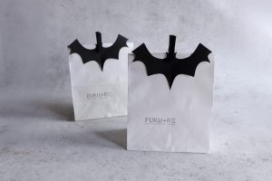 ハロウィンのお菓子ラッピングにぴったりな、黒いコウモリ飾りを付けた白い紙袋。シンプルで大人っぽいデザインのハロウィンラッピングアイデア。