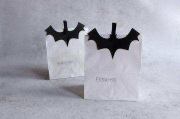 ハロウィンのお菓子ラッピングにぴったりな、黒いコウモリ飾りを付けた白い紙袋。シンプルで大人っぽいデザインのハロウィンラッピングアイデア。